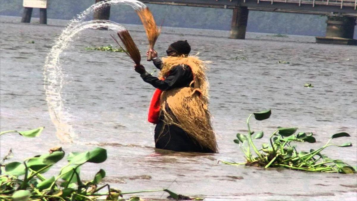 A person in a raffia costume standing in a river, splashing water.
