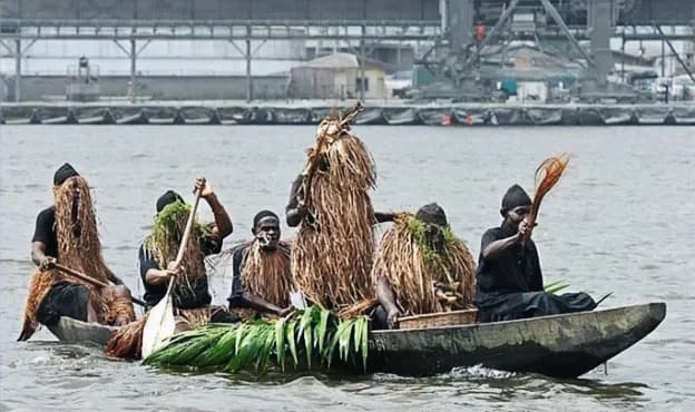 People in raffia costumes aboard a dugout canoe on the water.